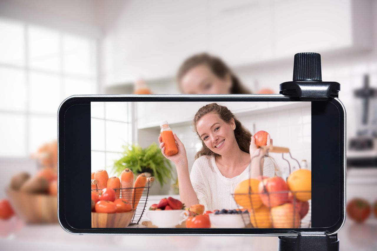 a woman taking a video shoot with her phone and promoting an orange beverage